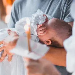 Dziecko w białej szacie trzymane na rękach, płonąca świeca.