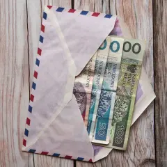 Koperta z pieniędzmi na drewnianym tle. Ile się daje na komunię świętą? W kopercie polskie banknoty: 50 i 100 zł.