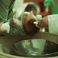 Chrzest dziecka: kapłan polewa głowę niemowlęcia wodą ze skorupki.