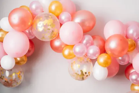 Girlanda z różowych, łososiowych, złotych i białych balonów, w tym kilka z konfetti.