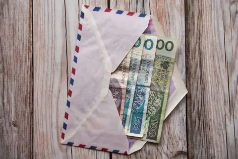 Koperta z pieniędzmi na drewnianym tle. Ile się daje na komunię świętą? W kopercie polskie banknoty: 50 i 100 zł.