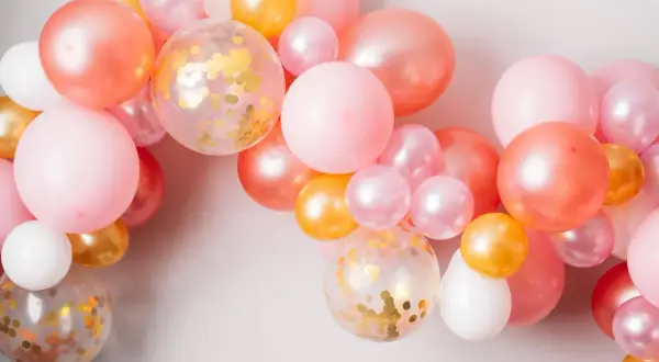 Girlanda z różowych, łososiowych, złotych i białych balonów, w tym kilka z konfetti.