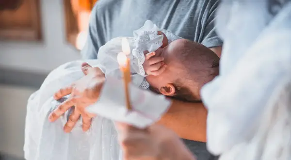 Dziecko w białej szacie trzymane na rękach, płonąca świeca.