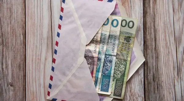 Koperta z pieniędzmi na drewnianym tle. Ile się daje na komunię świętą? W kopercie polskie banknoty: 50 i 100 zł.
