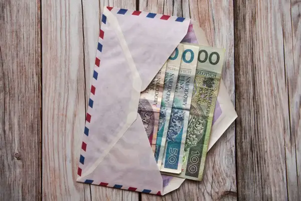 Koperta z pieniędzmi na drewnianym tle. Ile się daje na komunię świętą? W kopercie polskie banknoty: 50 i 100 zł.
